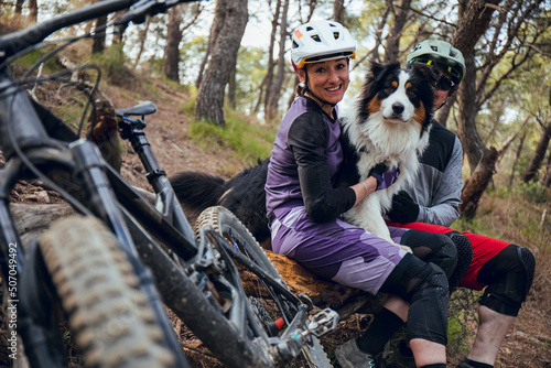 Close up of Family of enduro mtb riders with dog and bicycles in forest in summer