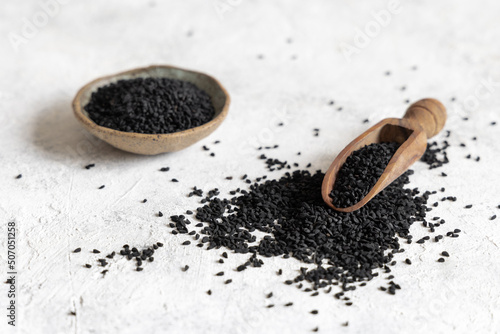 Scoop of Indian spice Black cumin (nigella sativa or kalonji) seeds on white table close up