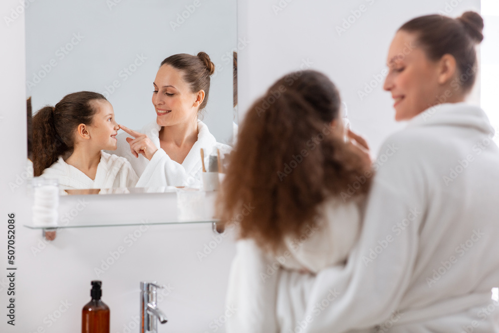 beauty, hygiene, morning and people concept - happy smiling mother and daughter looking to mirror at bathroom beauty, hygiene, morning and people concept - happy smiling mother and daughter looking to mirror at bathroom