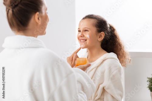beauty, hygiene, morning and people concept - happy smiling mother and daughter with moisturizer at bathroom