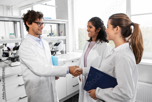 science, work and people concept - international group of happy scientists shaking hands in laboratory