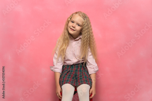 little girl schoolgirl sits in a chair. Pink background.