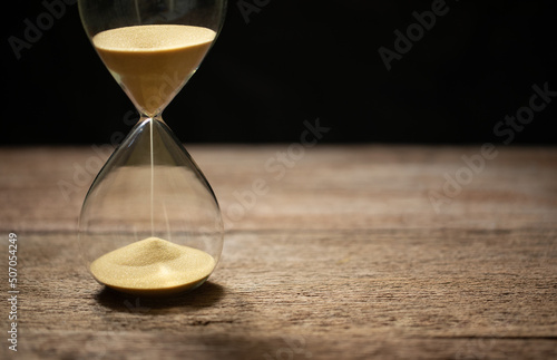 hourglass (sand clock) on an old wooden table with black background, deadline for doing business, elapsed time concept, copy space