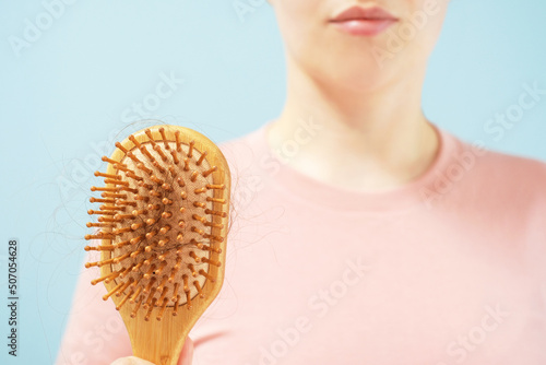 Young woman holding a comb with fallen hair close-up on blue background.