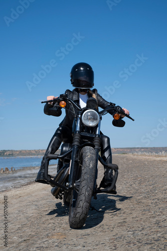 a girl biker in leather clothes and a black helmet rides on a stylish black motorcycle.