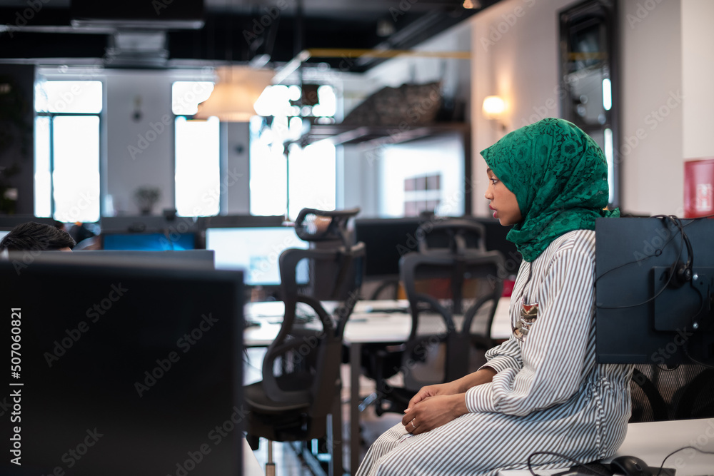  woman wearing a hijab on meeting in modern open plan office interior brainstorming, working on laptop and desktop computer. Selective focus 