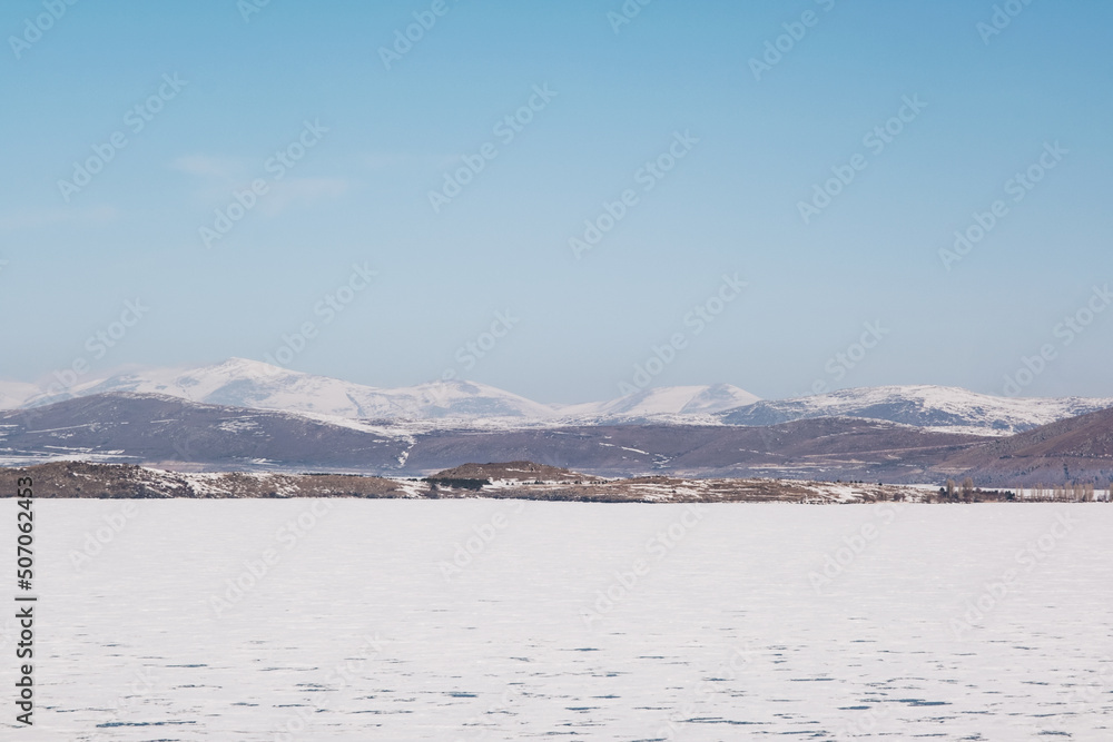 Landscape view of Frozen Cildir lake in Kars and snowy mountains with a blue sky in winter
