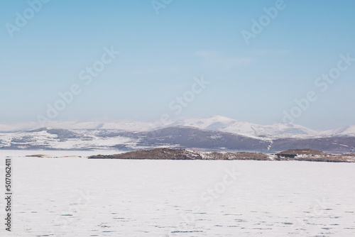Landscape view of Frozen Cildir lake in Kars and snowy mountains with a blue sky in winter © ardasavasciogullari
