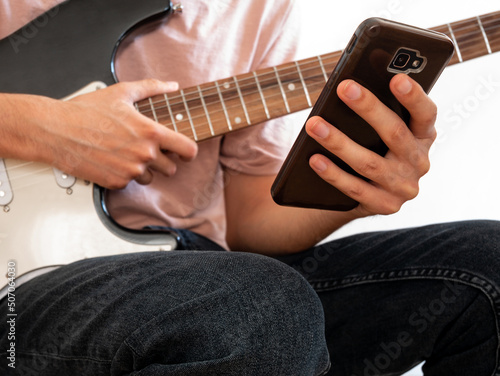 Young man learning to play the electric guitar through an app on his smartphone.