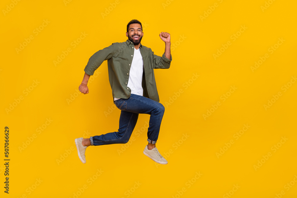 Full length photo of funky excited guy dressed green shirt jumping high running fast empty space isolated yellow color background