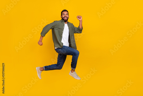 Full length photo of funky excited guy dressed green shirt jumping high running fast empty space isolated yellow color background