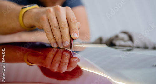 Process of pasting hood of red car with protective vinyl film from gravel chips and scratches. Transparent protection for paint