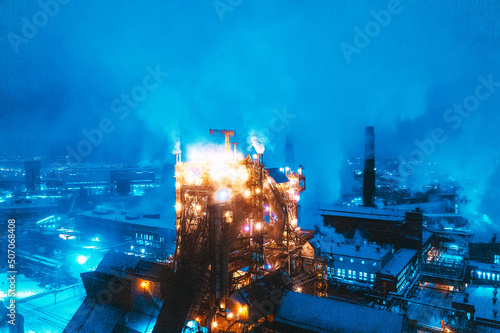 Night top view of steel plant at night with smokestacks and fire blazing out of the pipe. Industrial panoramic landmark with blast furnance of metallurgical production