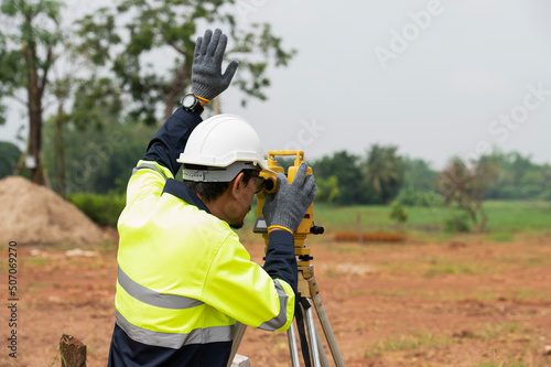 A young surveying engineer is measuring the level at a construction site. Surveyors certify accurate measurements before proceeding with the dormitory construction project.