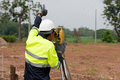 A young surveying engineer is measuring the level at a construction site. Surveyors certify accurate measurements before proceeding with the dormitory construction project.