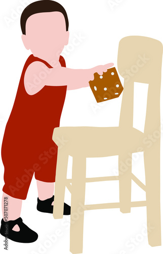 Child boy in red overalls stands near a wooden chair and holds a cube in his hand