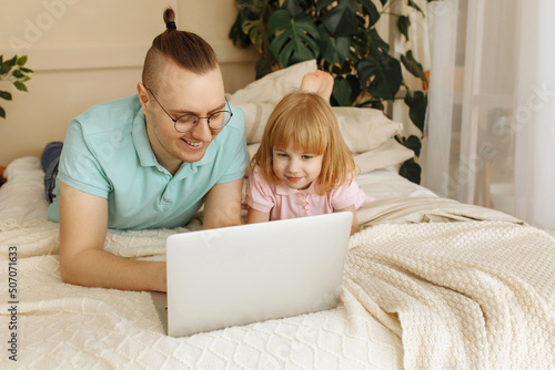 Dad and daughter lie on the bed and use a laptop