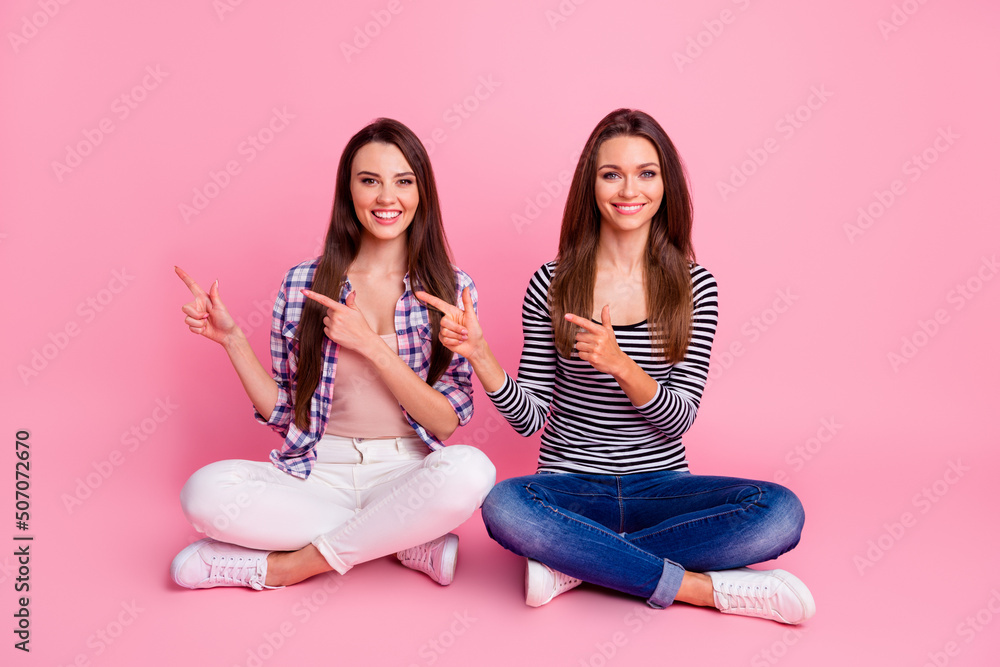 Full body photo of two pretty cheerful people sitting floor direct finger empty space isolated on pink color background