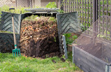 Open composting bin with fresh made compost, digging fork and sieve above raised bed ready to be planted