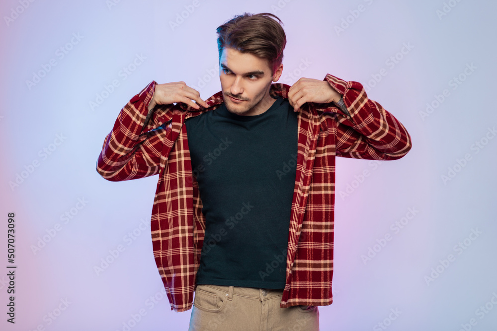 Stylish handsome brutal man with hair in a fashionable vintage clothing wears a plaid shirt in a studio with colored lights and pink-blue background Stylish handsome brutal man with hair in a fashionable vintage clothing wears a plaid shirt in a studio with colored lights and pink-blue background