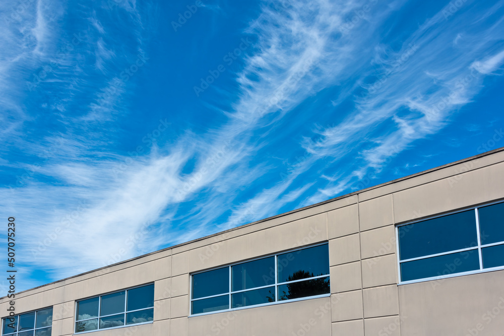 Fototapeta premium Top of the office building with windows on blue and cloudy sky background