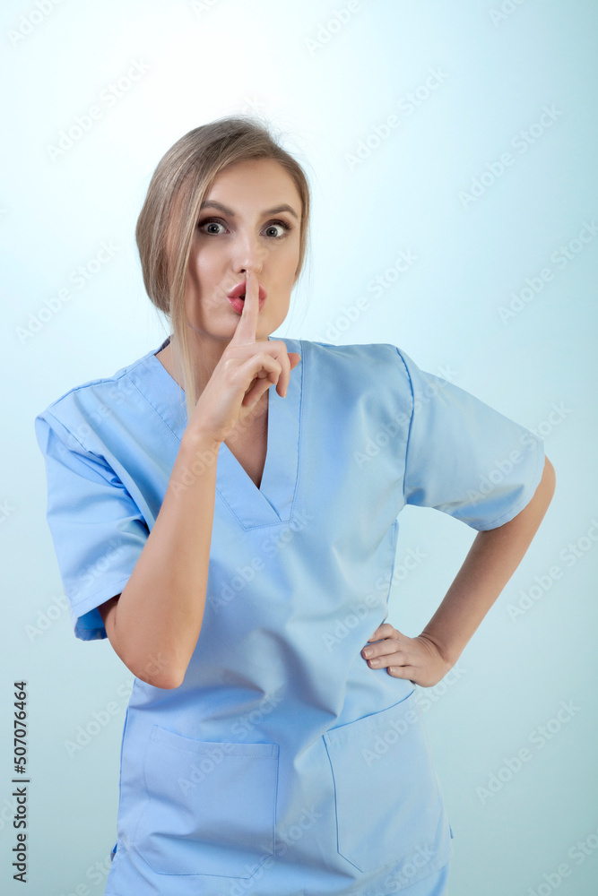 Young Female Nurse is Shushing Against Blue Background Young Female Nurse is Shushing Against Blue Background