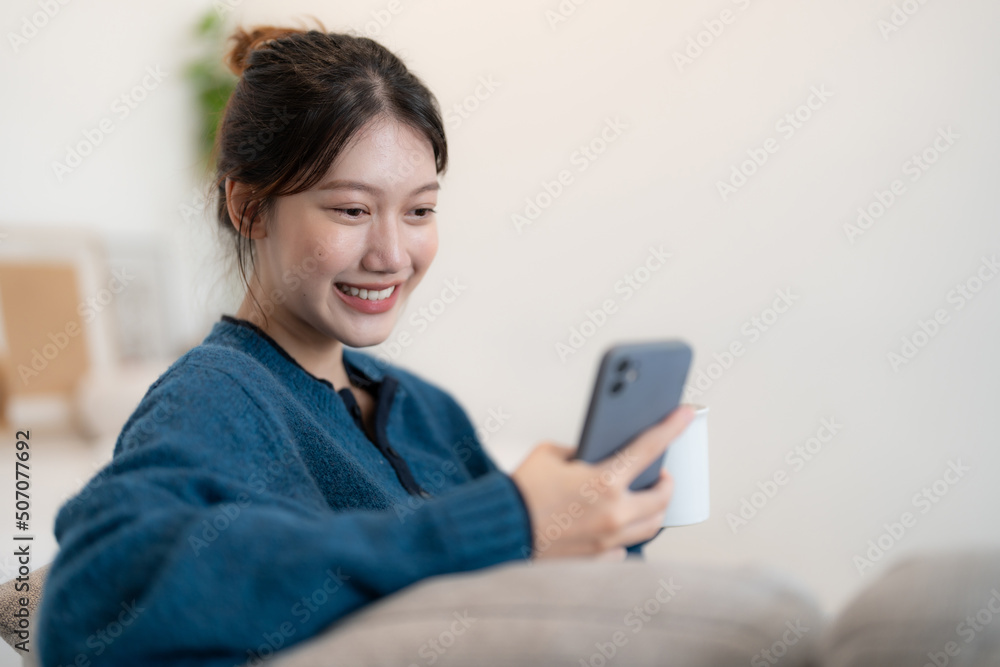 Happy young asian woman using mobile phone while sitting a couch at home Happy young asian woman using mobile phone while sitting a couch at home