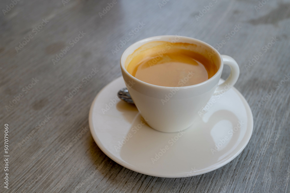Selective focus on coffee cup and saucer, Brown cream of black coffee in white mug on the wooden table with free copy space, Outdoor drinking warm drink in the afternoon. Selective focus on coffee cup and saucer, Brown cream of black coffee in white mug on the wooden table with free copy space, Outdoor drinking warm drink in the afternoon.