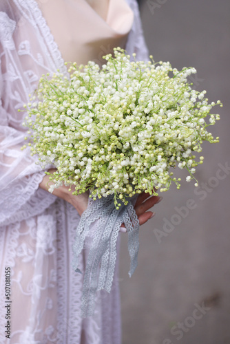 spring wedding bouquet of white lilies of the valley in the hands of the bride photo