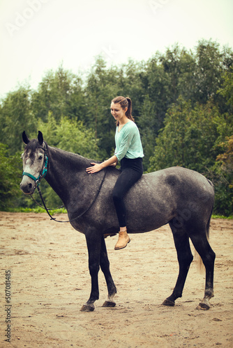 Young girl sits astride a grey horse.