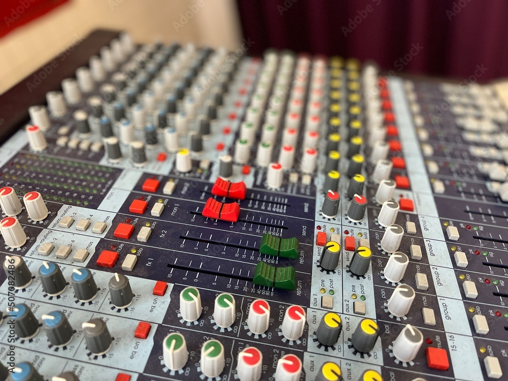 The surface of a sound mixer controller. Sound control panel is the essential tool of a sound engineer. Closeup of a mixing console against blurry background The surface of a sound mixer controller. Sound control panel is the essential tool of a sound engineer. Closeup of a mixing console against blurry background