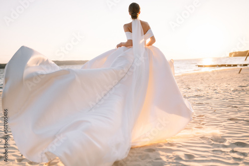 Foto Happy young bride woman in white dress running, have fun on clean sandy beach waves of azure sea or ocean on sunset, summer vacation at water