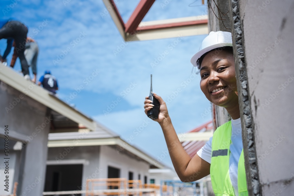 Cute face female engineer wearing a hard hat vest walkie-talkie wrench.a young woman with black skin is working happily.working safely Construction site management The back is of the construction.