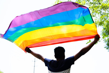 back view shot of young man proudly holding waving lgbtq flag - cocnept of pride month celebration, support and movement.