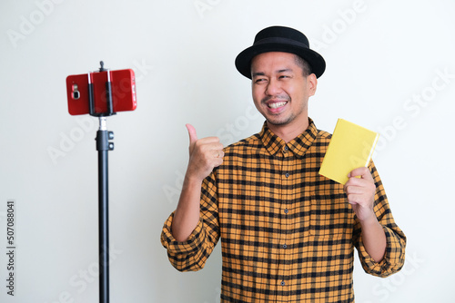 Adult Asian man smiling happy while showing a book during video call photo