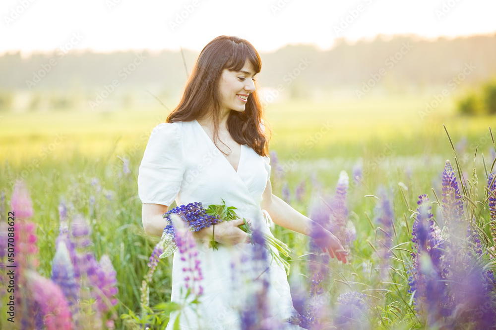 Beautiful woman in white sundress enjoying the summer nature. Picking colourful flowers, breathing fresh air and floral scent, walking in the sunny field of lupins. Happiness connect Beautiful woman in white sundress enjoying the summer nature. Picking colourful flowers, breathing fresh air and floral scent, walking in the sunny field of lupins. Happiness connect