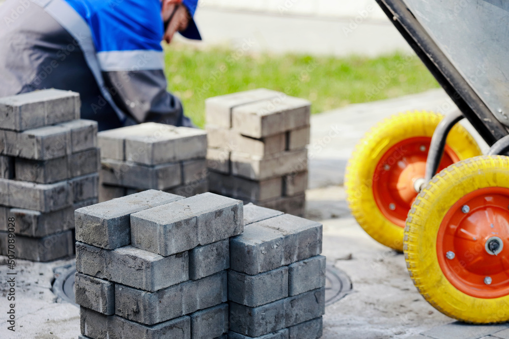 Bricklayer in work clothes sits on sidewalk and lays out paving slabs ...