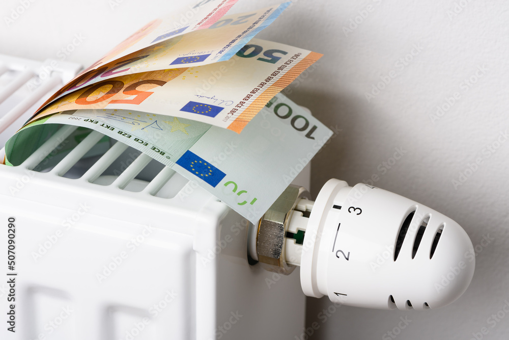 Euro money banknotes in heating radiator battery with thermostat temperature regulator. Concept of expensive heating costs and rising energy bill prices for winter cold season. Euro money banknotes in heating radiator battery with thermostat temperature regulator. Concept of expensive heating costs and rising energy bill prices for winter cold season.