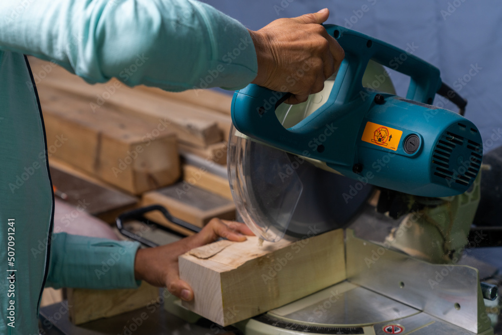 close-up of a woman carpenter cutting a block of wood with a chop saw
