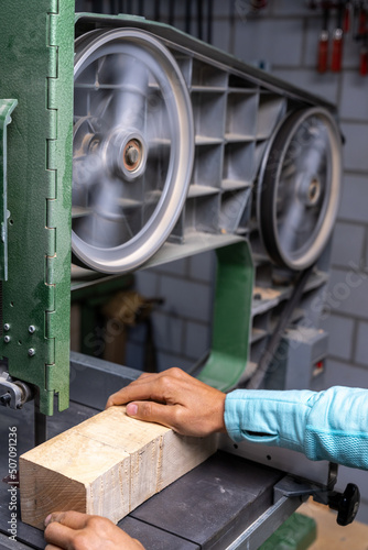 vertical close-up of a woman carpenter cutting a block of wood with a band saw photo