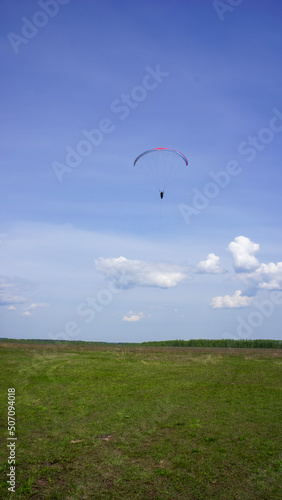 Paraglider flying in blue sky above green field in summer