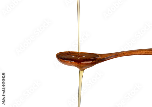 A thin jet of sunflower oil on a spoon and from a spoon on a white background.