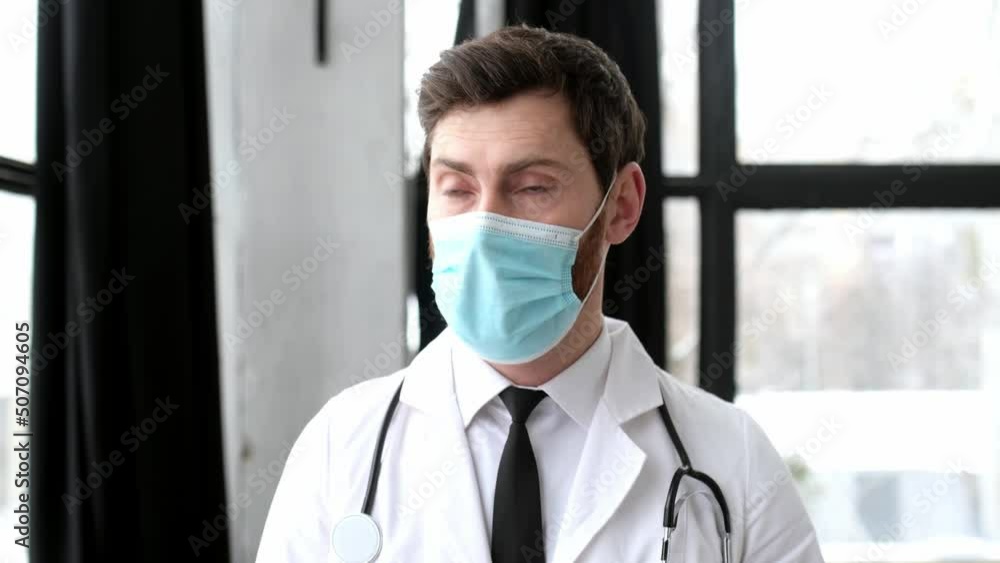Caucasian male doctor, therapist, surgeon, cardiologist in a medical uniform, protective mask and with stethoscope on shoulders, walks down the corridor of the hospital, take off medical mask, smiles Caucasian male doctor, therapist, surgeon, cardiologist in a medical uniform, protective mask and with stethoscope on shoulders, walks down the corridor of the hospital, take off medical mask, smiles