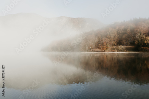A beautiful misty morning on lake Bohinj in Slovenia. Alpine autumn landscape with fog and calm lake. Lake fog sunrise with copy space. Brown tones tiny waves on the water. 