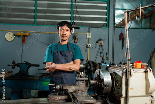 A young craftsman in a small family-owned factory, was carefully controlling the work of a lathe nearby.