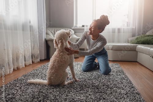 Cheerful happy young stylish woman laughing and playing with dog at home. Pet owner.