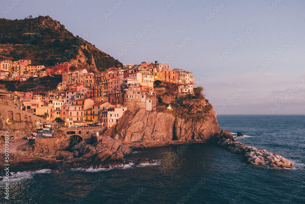 Beautiful view of rocky hills and colorful historic buildings of Manarola, tourist attraction and famous place in Liguria, Italy. Hillside over the sea at sunset.