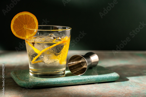 Glass of gin tonic with orange slice and ice. dark green background