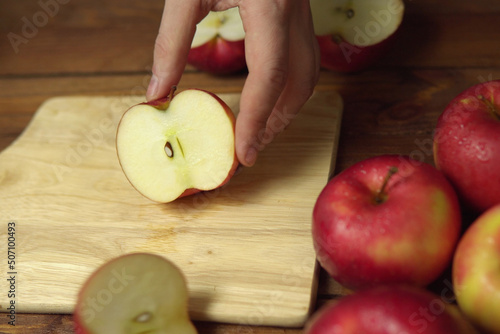 The hand holds half of the apple over the cutting board.