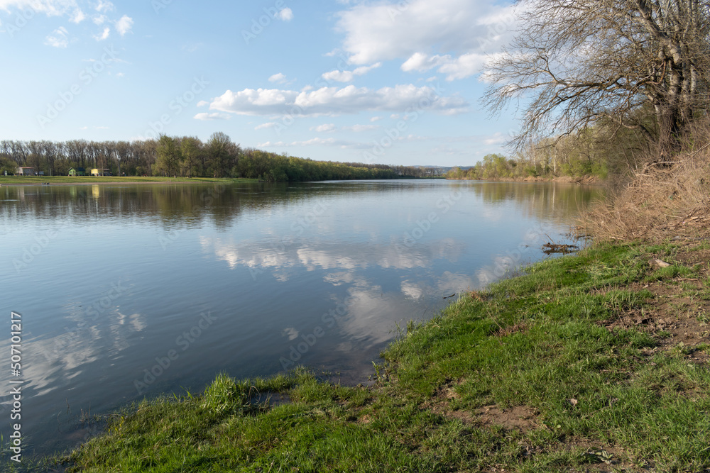 Calm scene of Sava river in spring, landscape of river with grassy shore and clouds in sky in spring